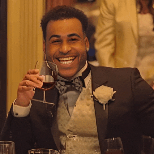 a man in a tuxedo is holding a glass of wine