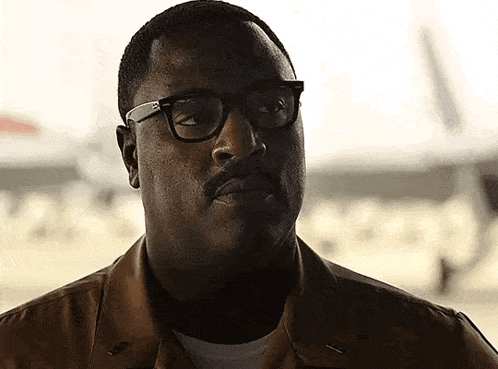 a man with glasses and a mustache is wearing a brown shirt
