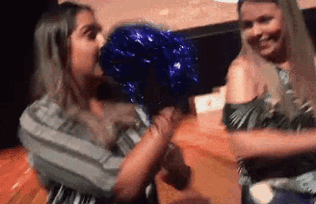 two women are standing next to each other holding a blue pom pom and smiling .