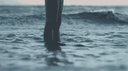 a woman is standing in the ocean on the beach .