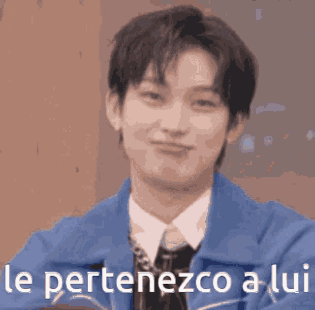 a man in a blue jacket and tie is making a funny face with the words le pertenezco a lui written below him .