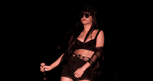 a woman in a crop top and shorts holds a microphone