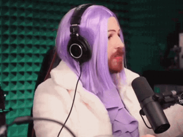 a man wearing a purple wig and headphones stands in front of a microphone