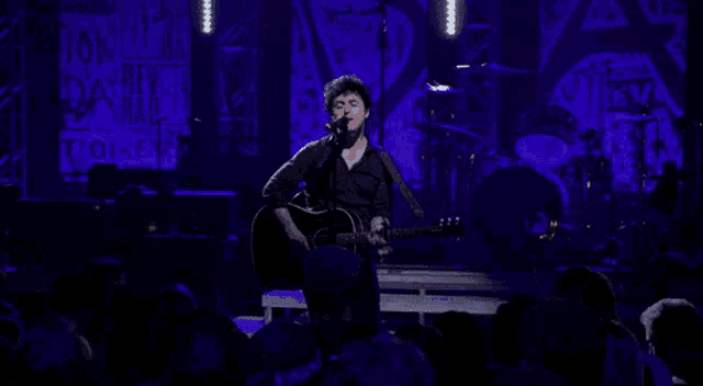 a man singing into a microphone while playing a guitar on stage