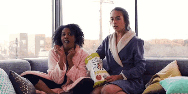 two women are sitting on a couch with a bag of popcorn