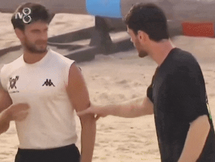 a man in a kappa shirt shakes hands with another man on the beach .