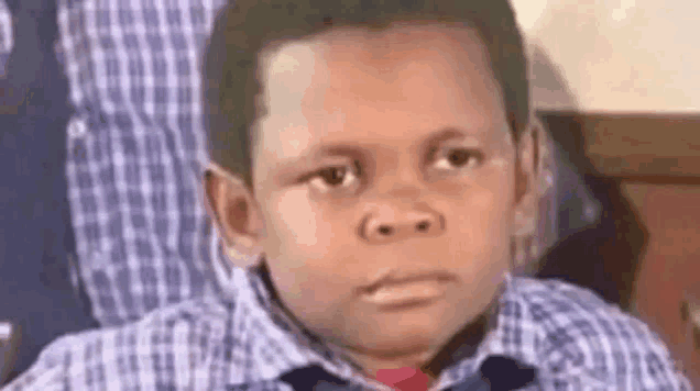 a young boy in a plaid shirt and tie is making a funny face while sitting in a chair .