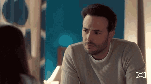 a man in a grey sweater looks at a woman in a room