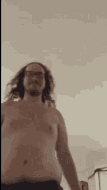 a shirtless man with long hair is standing in a room .