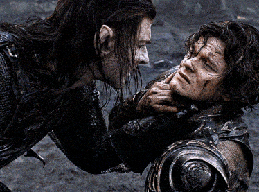 a man in armor is holding another man 's face in his hands