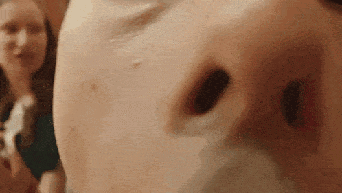 a close up of a person 's nose with a woman standing behind them .