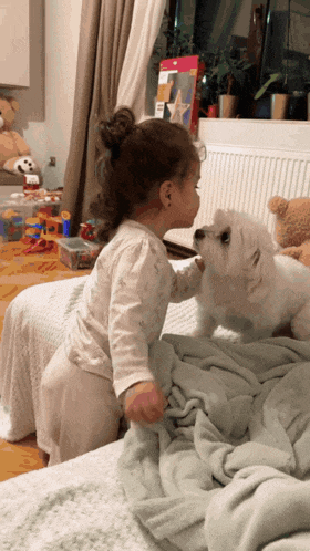 a little girl standing next to a white dog on a bed