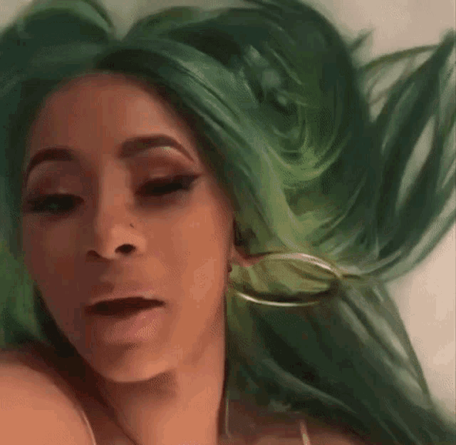a woman with green hair and hoop earrings is laying down .