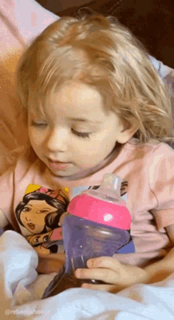a little girl is holding a purple bottle with a pink cap .