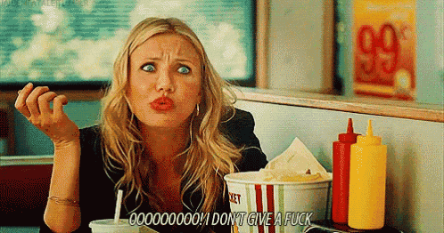 a woman is sitting at a table with a bucket of popcorn and a bottle of ketchup .