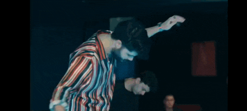 a man in a striped shirt is dancing with his arms outstretched .