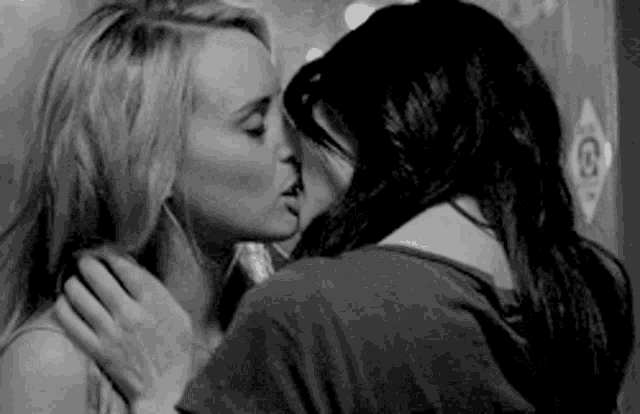 a couple of women are kissing in a black and white photo .