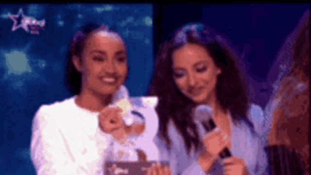 two women are standing next to each other on a stage and one is holding a microphone .