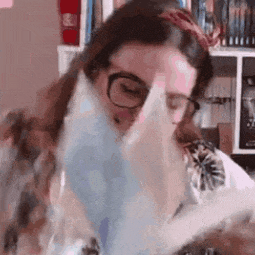 a woman wearing glasses is blowing a kiss while holding a book .