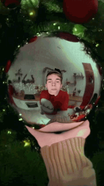 a person is holding a christmas ornament with a reflection of a person in it