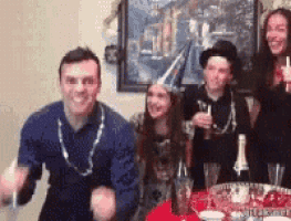 a group of people are standing around a table with a bottle of wine .