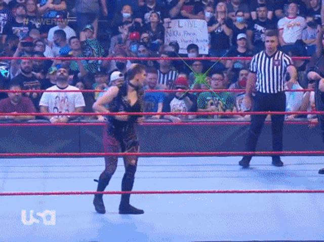 a wrestler is standing in a wrestling ring with a referee and a sign that says i love nikki