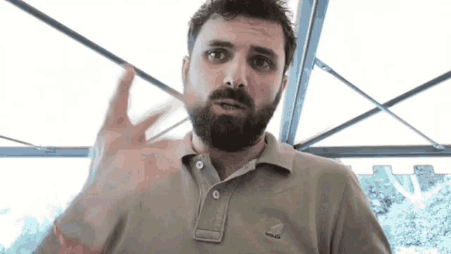 a man with a beard wearing a polo shirt is making a gesture with his hand