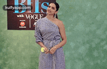 a woman in a blue and white dress is standing in front of a green wall holding a tennis racket .