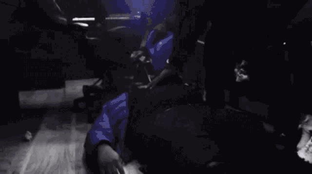 a man in a blue jacket is sitting in a dark room with a light shining on him .