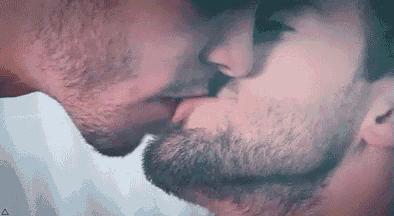 a man with a beard is kissing another man with his tongue out .