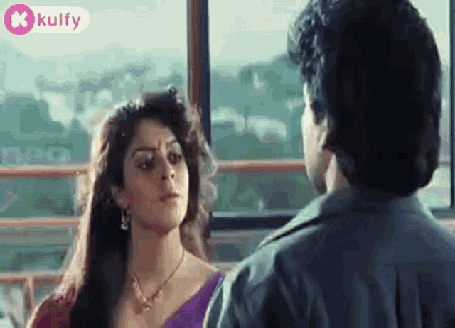 a man and a woman are standing next to each other and looking at each other in front of a window .