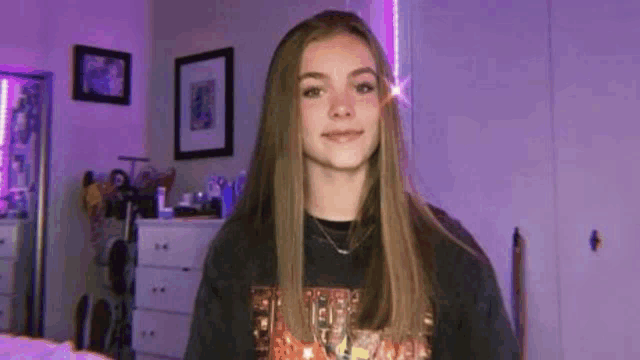 a young girl is standing in a room with purple lights on the walls and smiling .