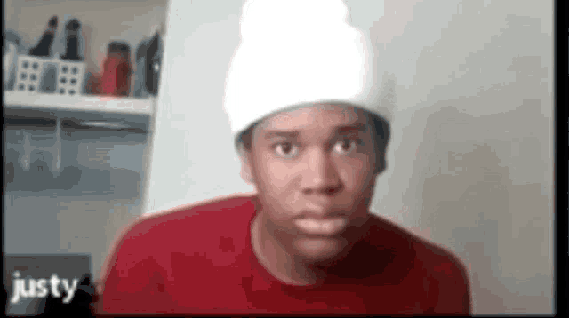a young man wearing a white hat and a red shirt is making a funny face .