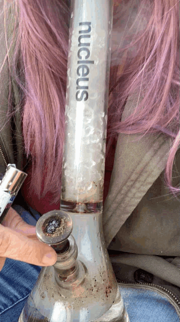 a woman with pink hair is smoking a nucleus bong