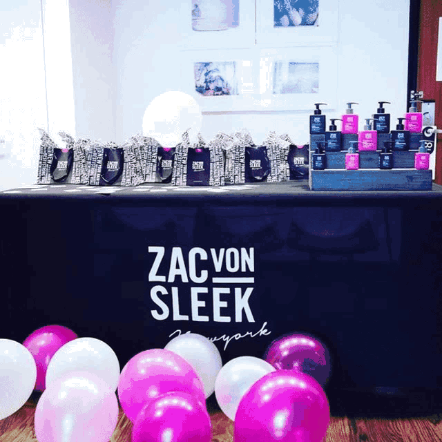 a table with pink and white balloons and a sign that says zac von sleek on it
