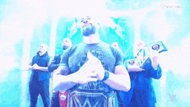 a man with a beard is holding a wrestling championship belt while standing in front of a group of men .