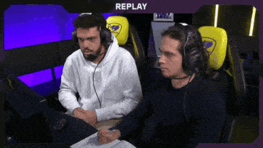 two men wearing headphones are sitting in front of a replay screen