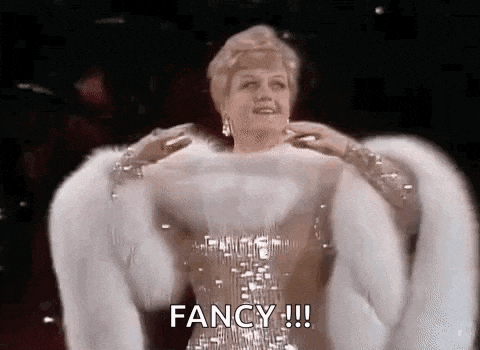 a woman in a fur coat is standing on a stage and says `` fancy '' .