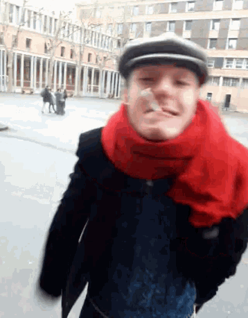 a man wearing a hat and a red scarf looks at the camera