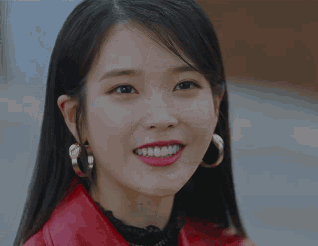 a woman wearing hoop earrings and a red jacket sticks her tongue out