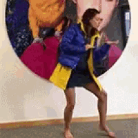 a woman in a blue jacket and yellow skirt is standing in front of a large painting of a woman .