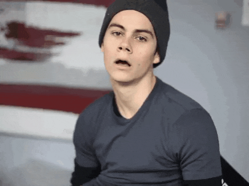 a young man wearing a hat and a t-shirt is making a funny face