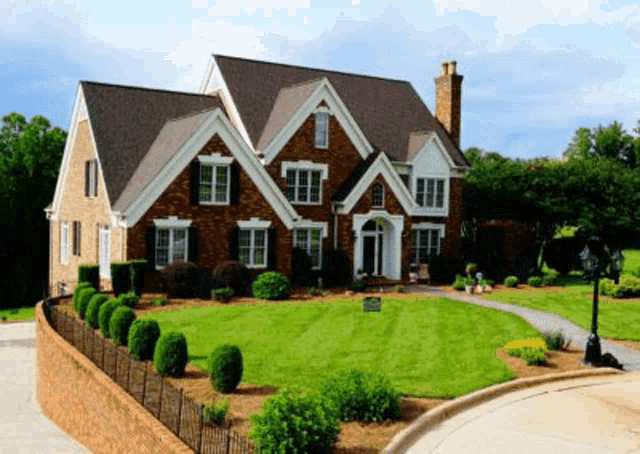 a large brick house with a fence around it and a lush green lawn
