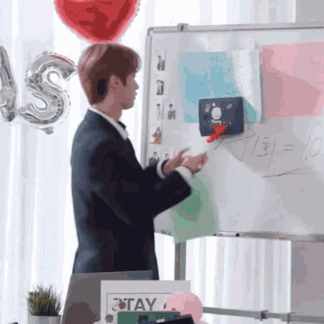 a man in a suit stands in front of a whiteboard with the numbers 7 31 = 19 on it