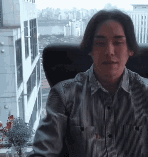 a man wearing a striped shirt is sitting in a chair with his eyes closed