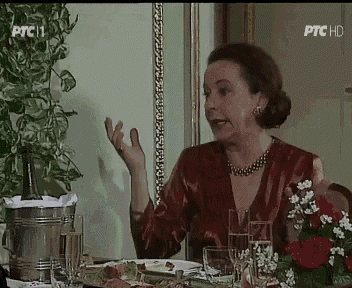 a woman in a red dress is sitting at a table with a bucket of champagne and glasses of wine ..