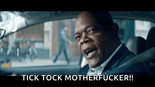 a man in a suit is driving a car and making a funny face with the words tick tock motherfucker .