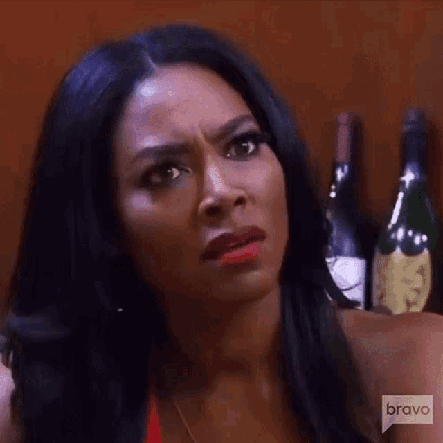 a woman is making a funny face while sitting in front of a row of wine bottles .