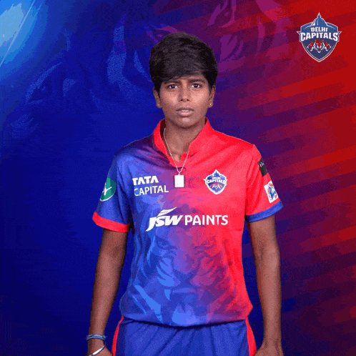 a man wearing a delhi capitals jersey holds his fist up in the air
