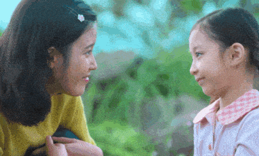 a woman in a yellow sweater talks to a little girl in a pink shirt